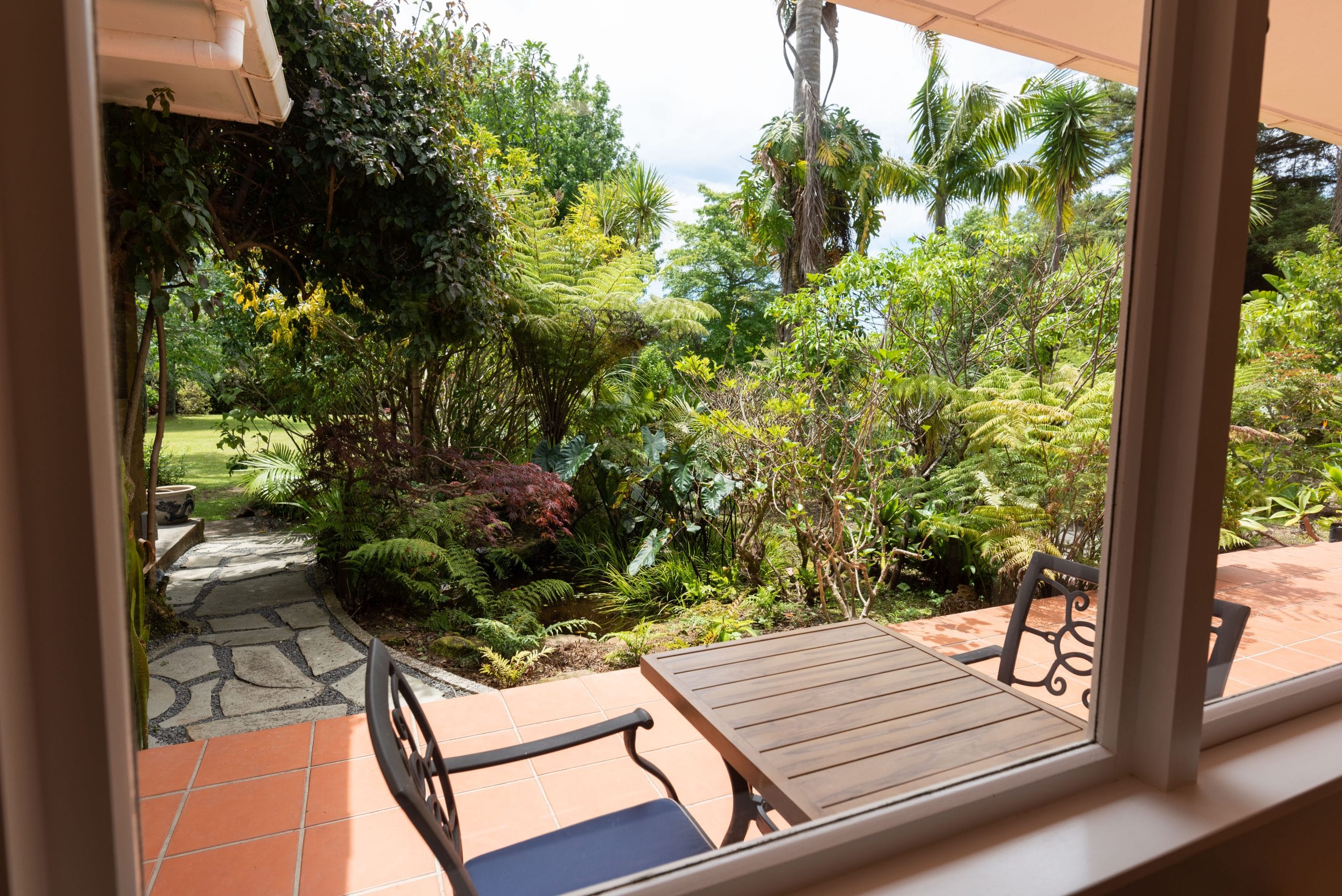 View of the subtropical gardens and guest patio from the Kotarē room at Pāteke Lodge.