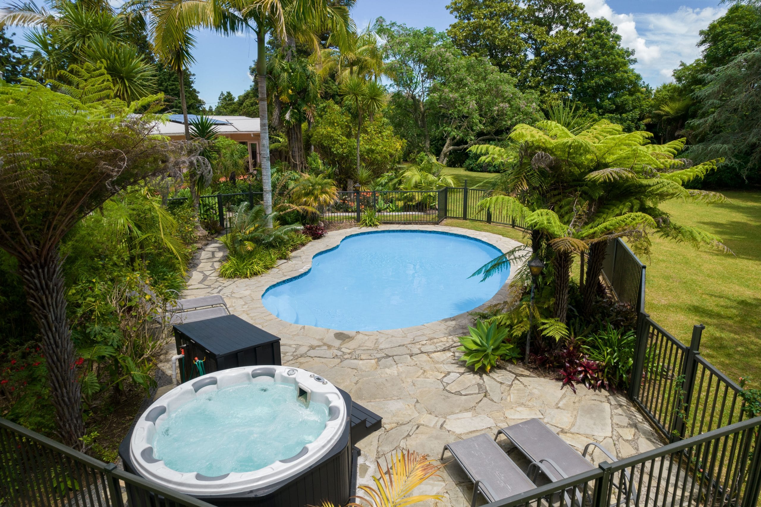 Outdoor hot tub and swimming pool amongst lush subtropical gardens at Pāteke Lodge, Kerikeri.